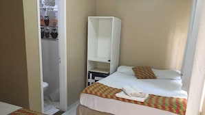 Une chambre d’hôtel avec un lit, une armoire et une salle de bain visible à travers une porte ouverte.