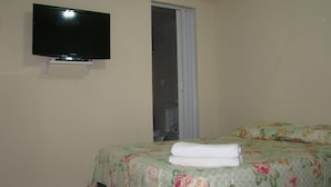 Une chambre à coucher avec un lit, un téléviseur fixé au mur et une fenêtre avec des rideaux.