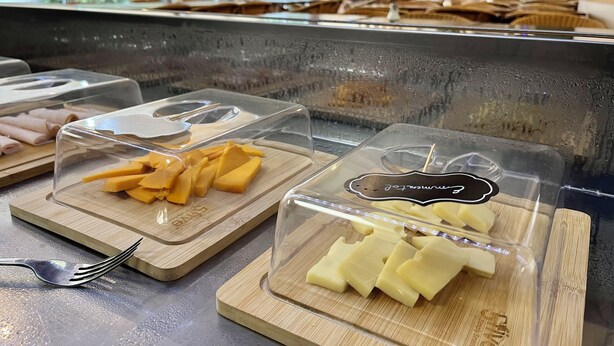 A buffet with various food items in clear containers, including sliced cheese and meat, on wooden serving boards. - Auberge de jeunesse HI Bordeaux-Blanquefort (Ex Otellia) (Blanquefort)