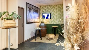 A modern interior with a green textured wall, a mounted television, a wooden barrel, and a wicker basket on a table. - Auberge de jeunesse HI Bordeaux-Blanquefort (Ex Otellia) (Blanquefort)