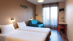 A hotel room with two beds, a desk, a chair, a TV, and a window with curtains. - Auberge de jeunesse HI Bordeaux-Blanquefort (Ex Otellia) (Blanquefort)