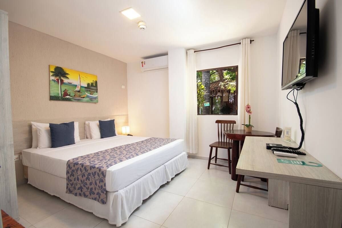 Hotelkamer met een bed, bureau, stoel, televisie en een schilderij aan de muur.