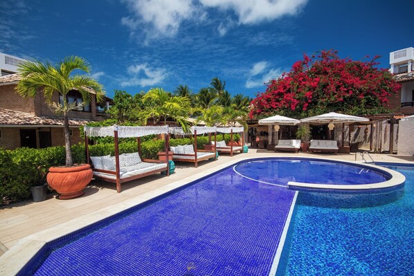 Ein Poolbereich mit einem blau gefliesten Pool, Liegestühlen und einer Palme.