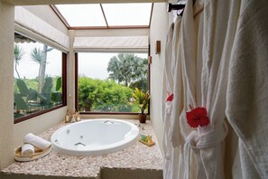 Ein Badezimmer mit einer großen Badewanne, einem Fenster mit Blick auf Grünflächen und einem Handtuchhalter mit einer roten Blume.