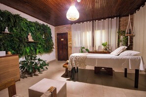 Ein Zimmer mit einem Bett, einer Holzkommode, einem kleinen Tisch und einer hängenden Makramee-Pflanze.