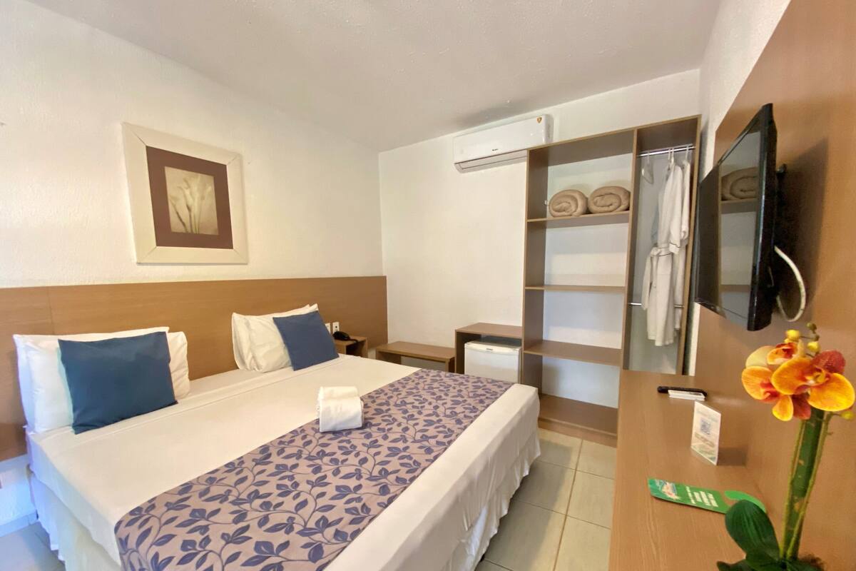 Een hotelkamer met een bed, bureau, stoel, televisie, airconditioning, kledingkast en een potplant.