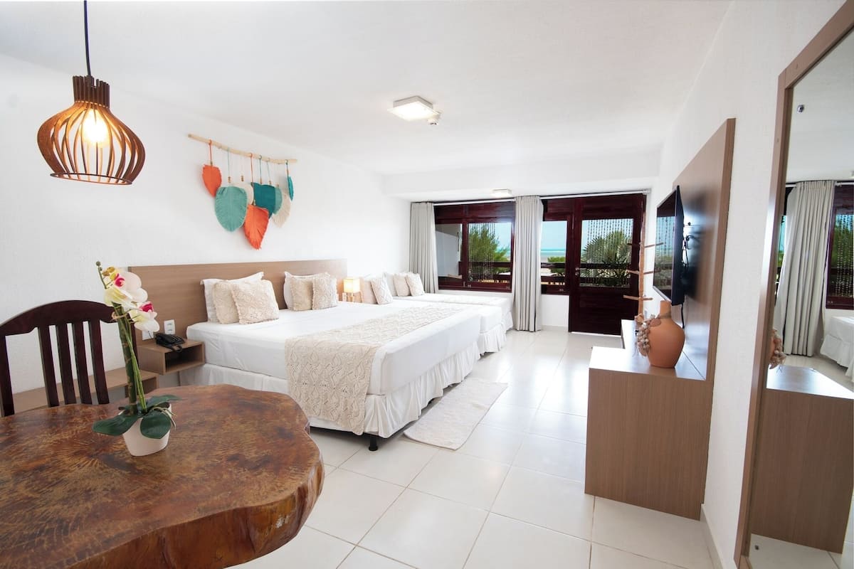 Een moderne hotelkamer met een groot bed, een eettafel met een bloemenvaas, een houten bijzettafeltje en een televisie op een standaard.