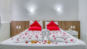 A hotel room with a neatly made bed, red pillows, and rose petals arranged on the bed. - Praia Hotel Enseada (Maceió)
