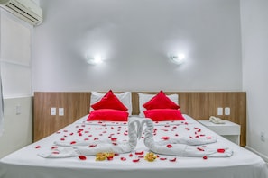 A hotel room with a neatly made bed, red pillows, and rose petals arranged on the bed. - Praia Hotel Enseada (Maceió)