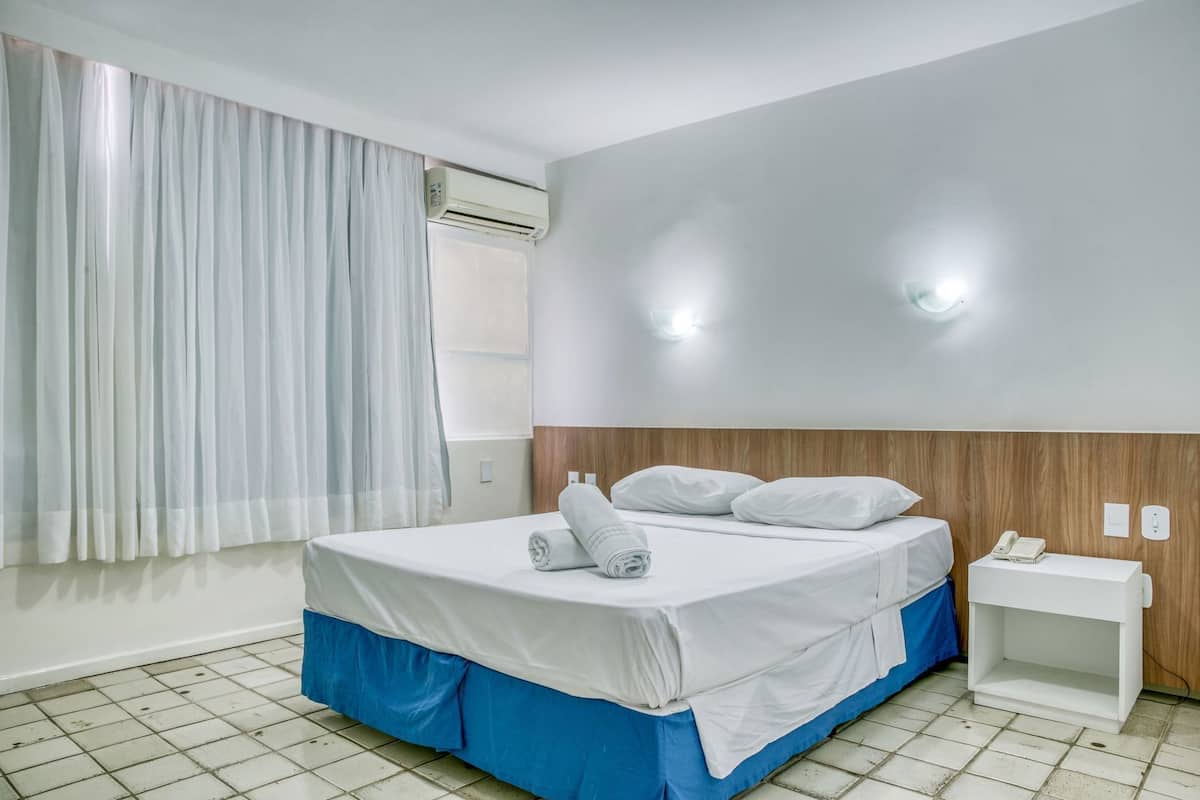 Ein Hotelzimmer mit einem Bett, einem Nachttisch mit Telefon und einer Klimaanlage.