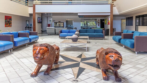 A spacious lobby with blue sofas and armchairs, a central coffee table, and two lion statues. - Praia Hotel Enseada (Maceió)