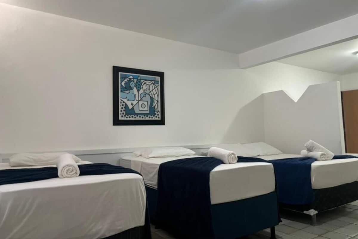 Ein Hotelzimmer mit zwei Einzelbetten, weißer Bettwäsche, einem blauen abstrakten Gemälde an der Wand und einer Deckenleuchte.