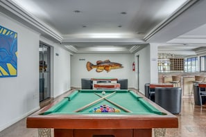 Una mesa de billar con un mural de peces, una zona de bar y un área de estar con sillas.