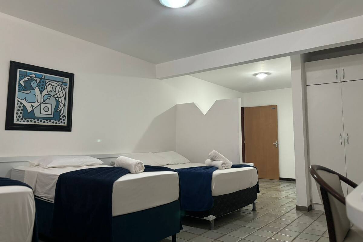 Ein Hotelzimmer mit zwei Betten, einer Deckenleuchte, einem gerahmten Kunstwerk und einem Kleiderschrank.