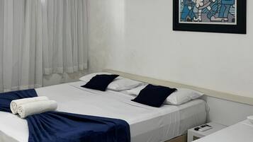 Habitación de hotel con dos camas, sábanas blancas, colchas azul oscuro, almohadas blancas, un cuadro enmarcado en la pared y una cortina blanca.