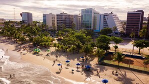 A beach with palm trees, umbrellas, and people. - Praia Hotel Enseada (Maceió)
