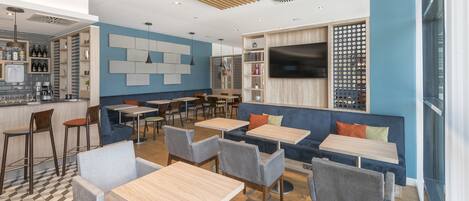 A modern cafe with wooden tables and chairs, a bar area, and a large TV screen.