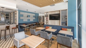 Um café moderno com mesas e cadeiras de madeira, um balcão e uma grande tela de televisão.