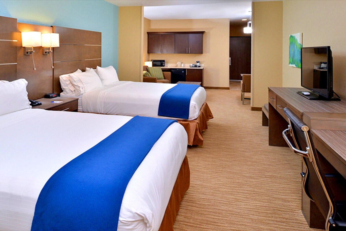 A hotel room with two beds, a desk, a chair, a microwave, and a television.
