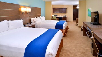 Quarto de hotel com duas camas, uma mesa, uma cadeira, micro-ondas e uma pequena cozinha.
