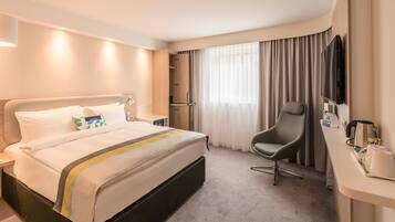 A hotel room with a bed, a desk with a chair, a TV, and a coffee maker.