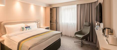A hotel room with a bed, a desk with a chair, a TV, and a coffee maker.