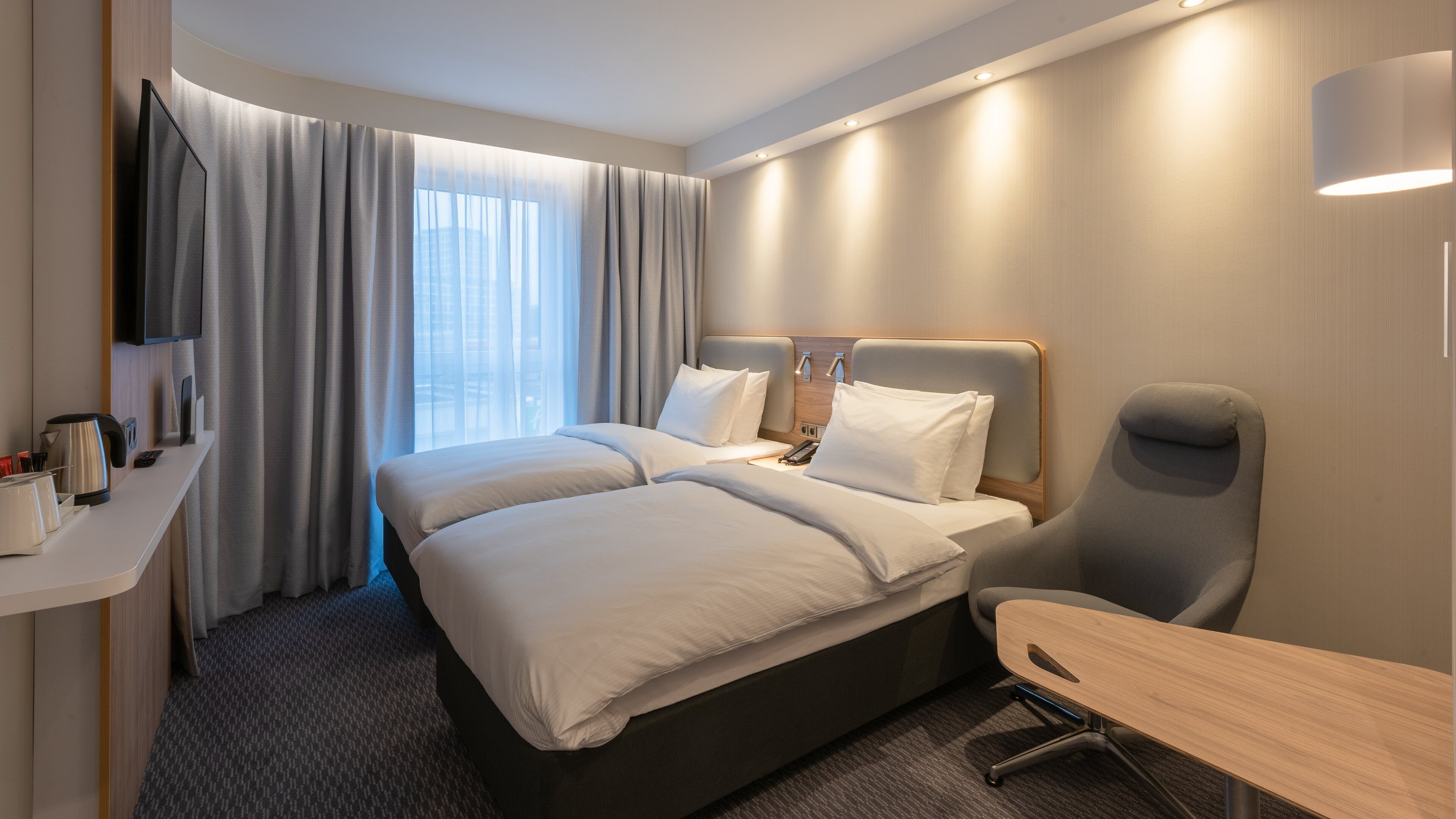 A modern hotel room with a large bed, a desk, and a chair.