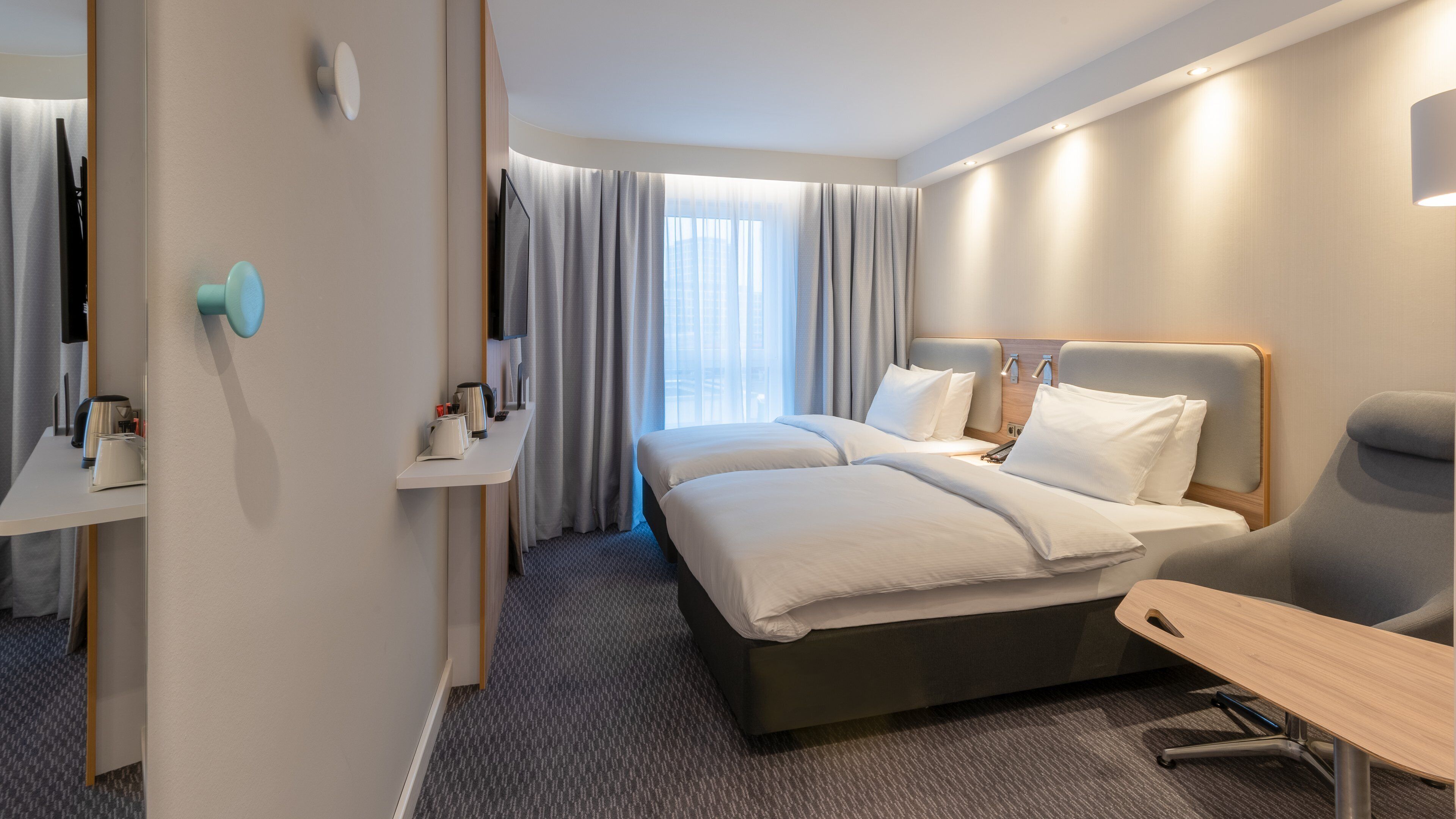 A modern hotel room with a large bed, a desk, and a mirror.