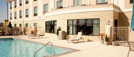 A hotel with a swimming pool, outdoor seating, and a stone facade.