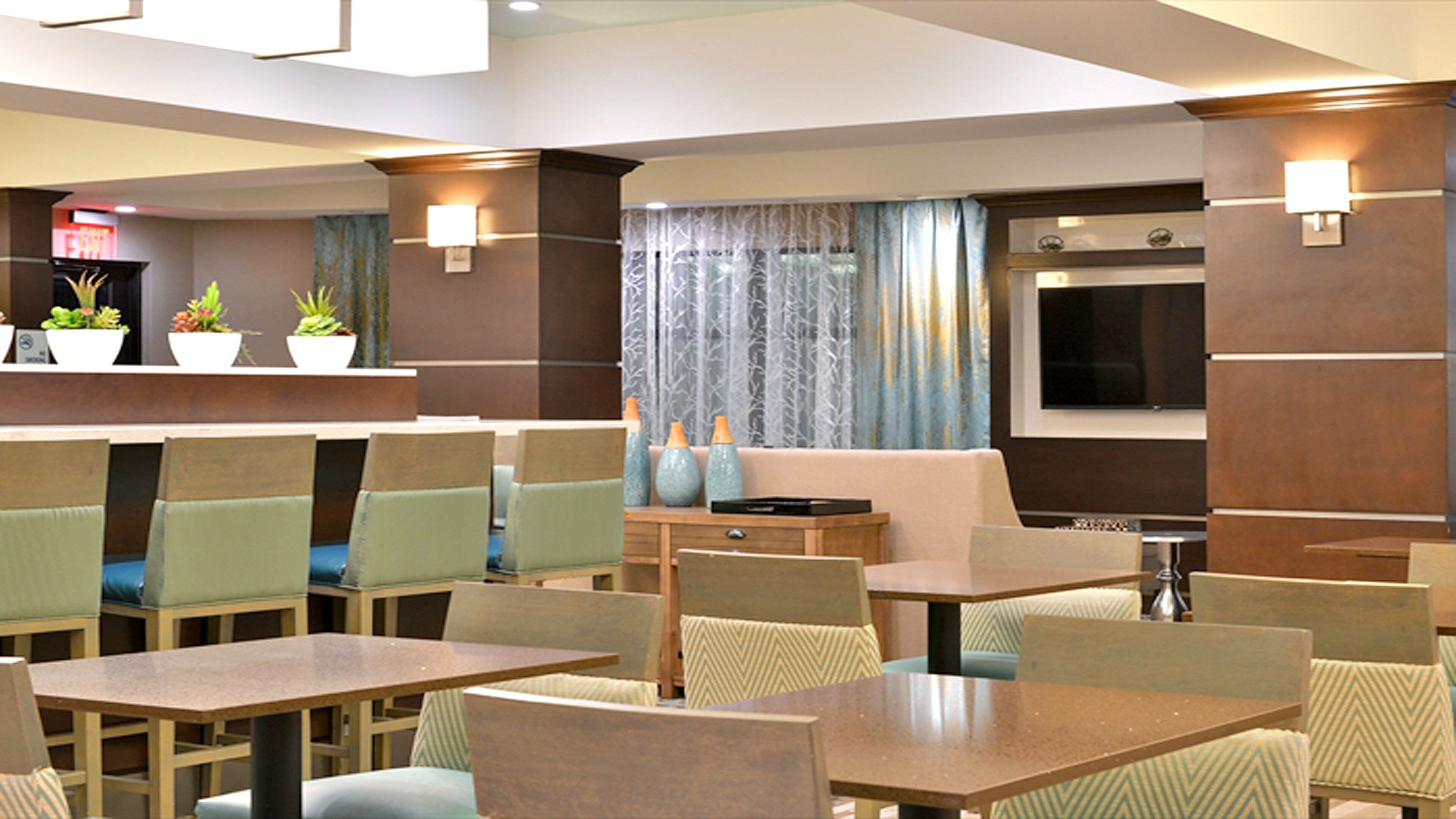 A hotel lobby with multiple seating areas, a reception desk, and a television screen.