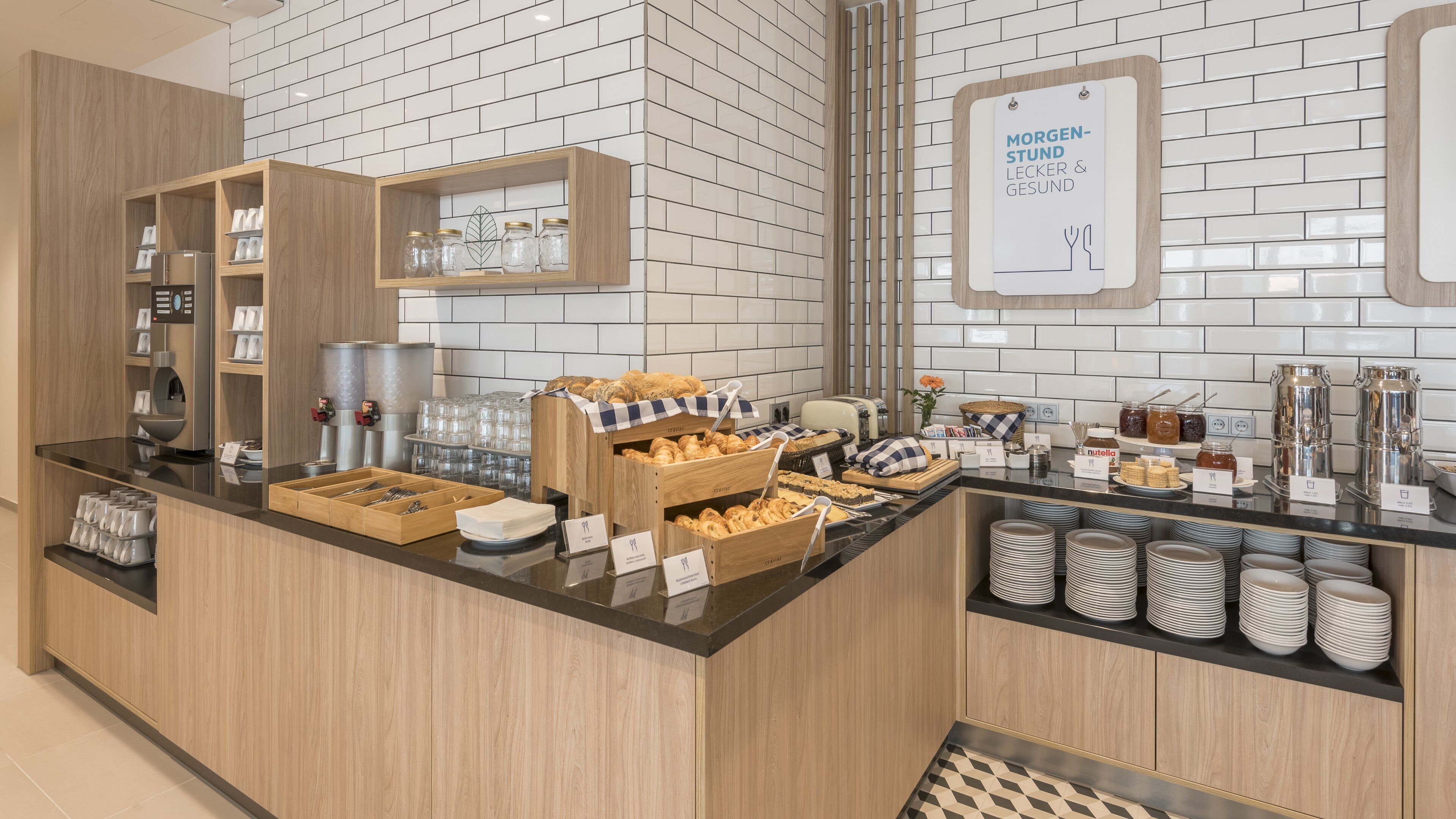A breakfast buffet area with various food items, a coffee machine, and a sign indicating "Morgen-Stund Lecker & Gesund".