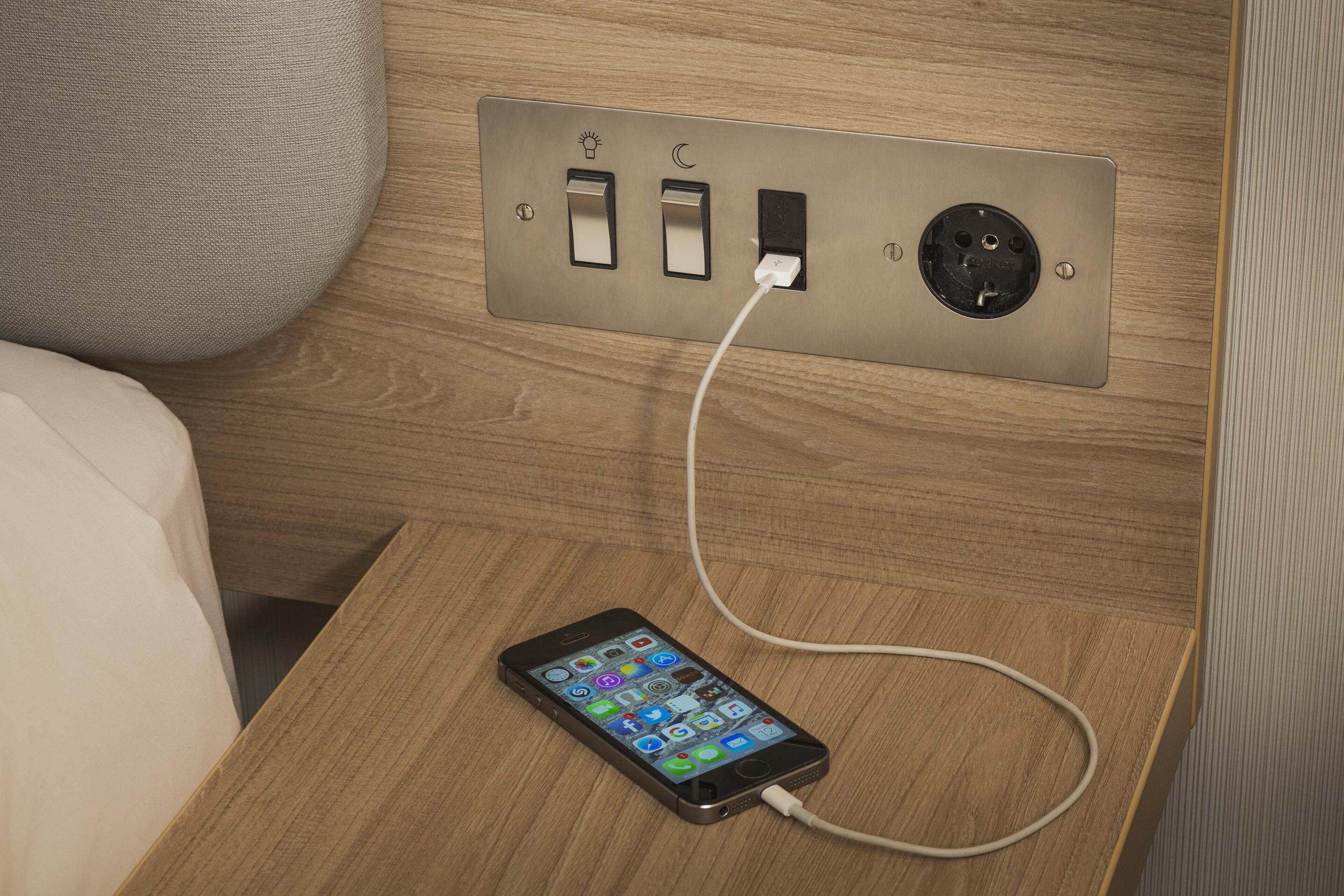 A smartphone charging on a wooden nightstand with a wall socket.
