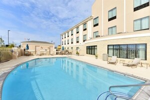 Piscina com espreguiçadeiras e um edifício com várias janelas e varandas.