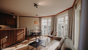 A modern living room with a wooden dining table, a sofa, and a kitchen area with wooden cabinets and a built-in bench. - Villa Usedom (Heringsdorf)