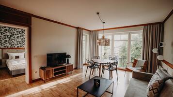 Una sala moderna con piso de madera, un sofá, un televisor, una mesa de comedor con sillas y un balcón con cortinas.