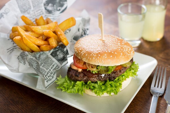 Una hamburguesa con pan de sésamo, lechuga, tomate y una hamburguesa de carne, acompañada de papas fritas sobre un plato blanco.