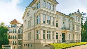 A multi-story building with a classical architectural style, featuring a prominent entrance with a green door and a balcony. - Villa Usedom (Heringsdorf)