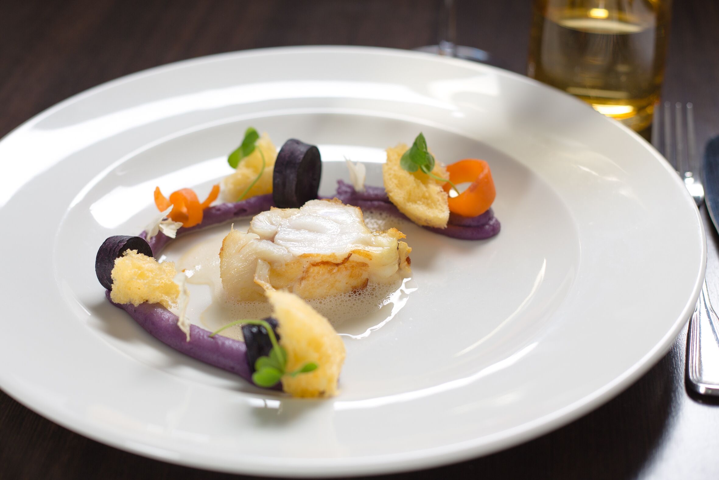 Un piatto bianco con un pezzo di pesce, verdure viola e guarnizioni.