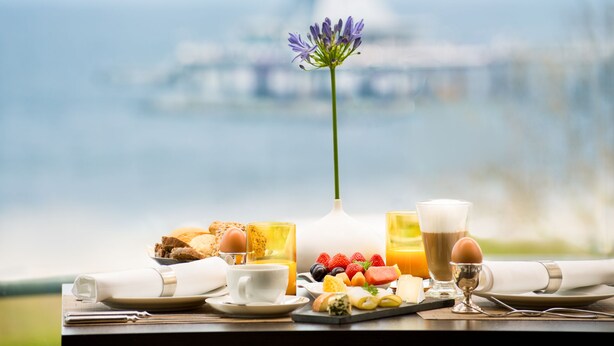 A breakfast setup with a variety of foods and drinks on a table, overlooking a body of water. - Villa Usedom (Heringsdorf)