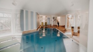 A swimming pool with a tiled floor, a lounge area with chairs, and a view of the outdoors through large windows. - Villa Usedom (Heringsdorf)