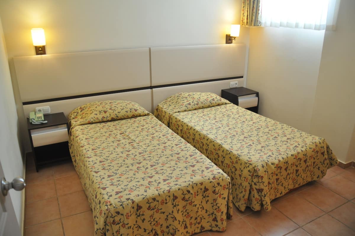 A hotel room with two single beds, each with a floral bedspread, a nightstand with a lamp, and a telephone.