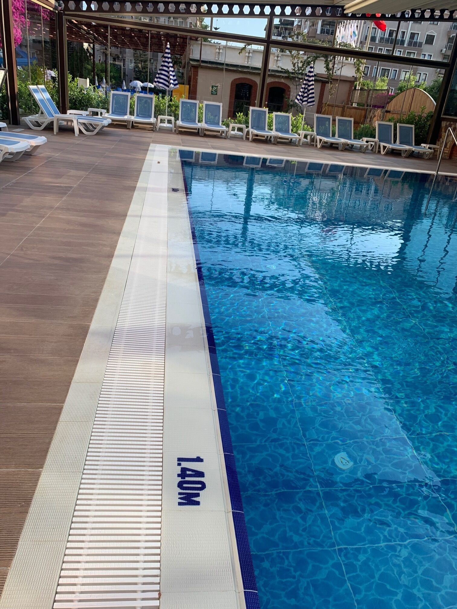 Une piscine à l’eau d’un bleu limpide, dont la profondeur est clairement indiquée (1,40 mètre), entourée de chaises longues et de parasols.