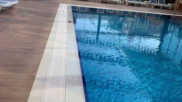 Une piscine à l’eau d’un bleu limpide, dont la profondeur est clairement indiquée (1,40 mètre), entourée de chaises longues et de parasols.