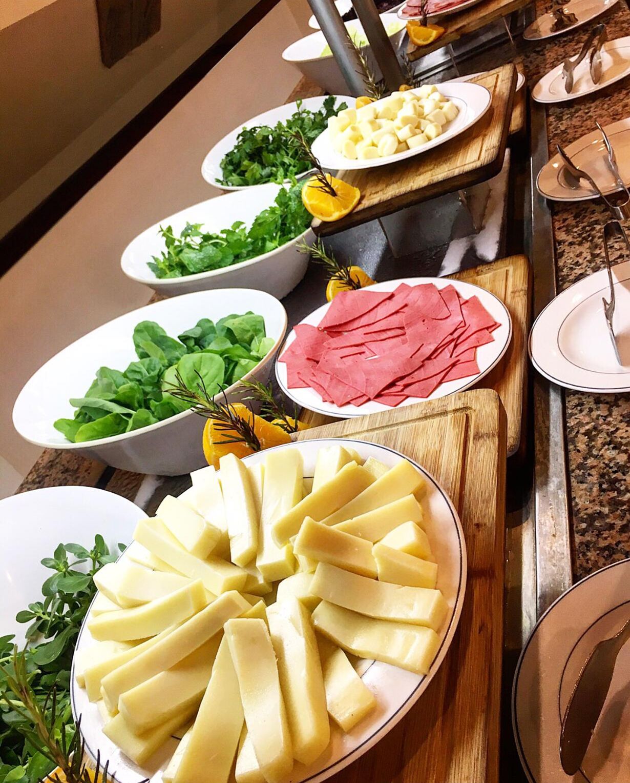 A buffet table with various food items including sliced cheese, leafy greens, and sliced meat.
