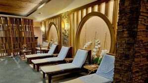 Un área de spa con tumbonas de madera, paredes de piedra y arcos decorativos.