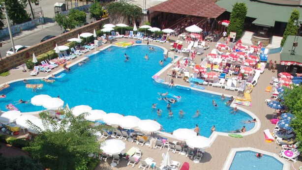 Una amplia piscina al aire libre con varias pistas de natación, rodeada de sillas de descanso y sombrillas.