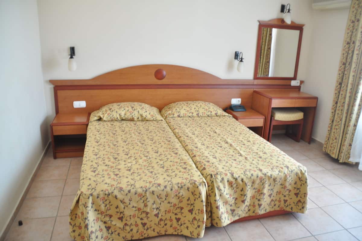 A double bed with floral bedding, a wooden nightstand, a small table with a chair, a mirror, and a wall-mounted light fixture.