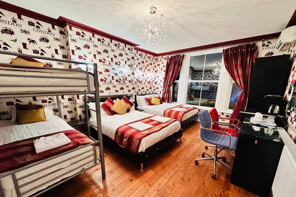 A hotel room with two beds, a desk, a chair, a chandelier, and a window with curtains.