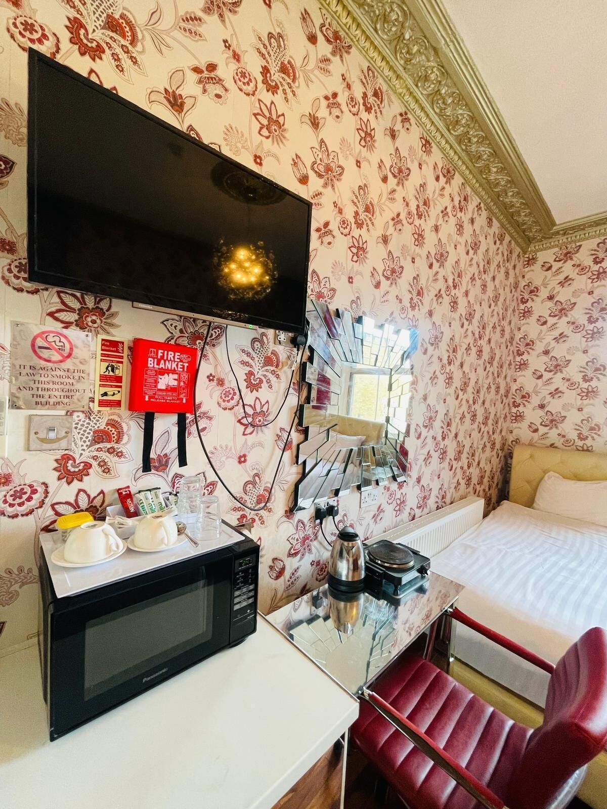 Une chambre d’hôtel équipée d’un lit, d’un fauteuil rouge, d’un four à micro-ondes, d’une machine à café et d’un téléviseur fixé au mur.
