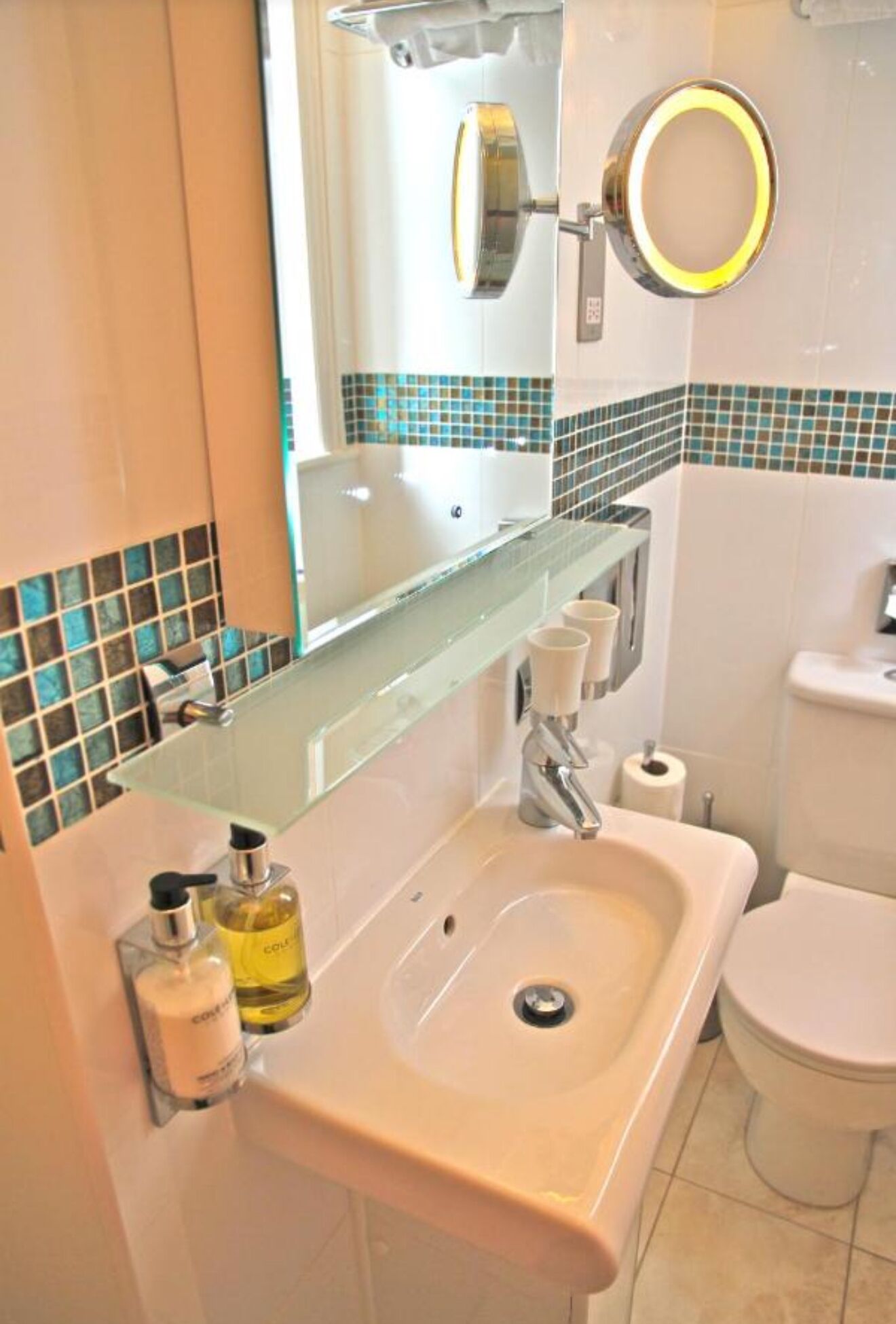 Een badkamer met een wastafel, spiegel, toilet en een betegelde spatwand.
